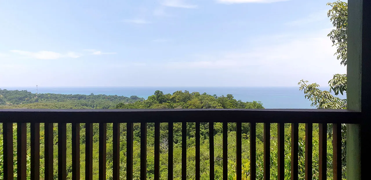 View from a timber balcony over green treetops to the blue Caribbean Sea